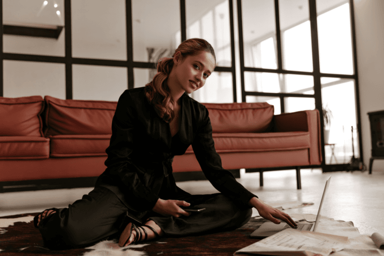 Confident woman in a black outfit working on a laptop while seated on the floor in a modern office, symbolizing strategic planning, entrepreneurship, and business growth lawyers legal jargon