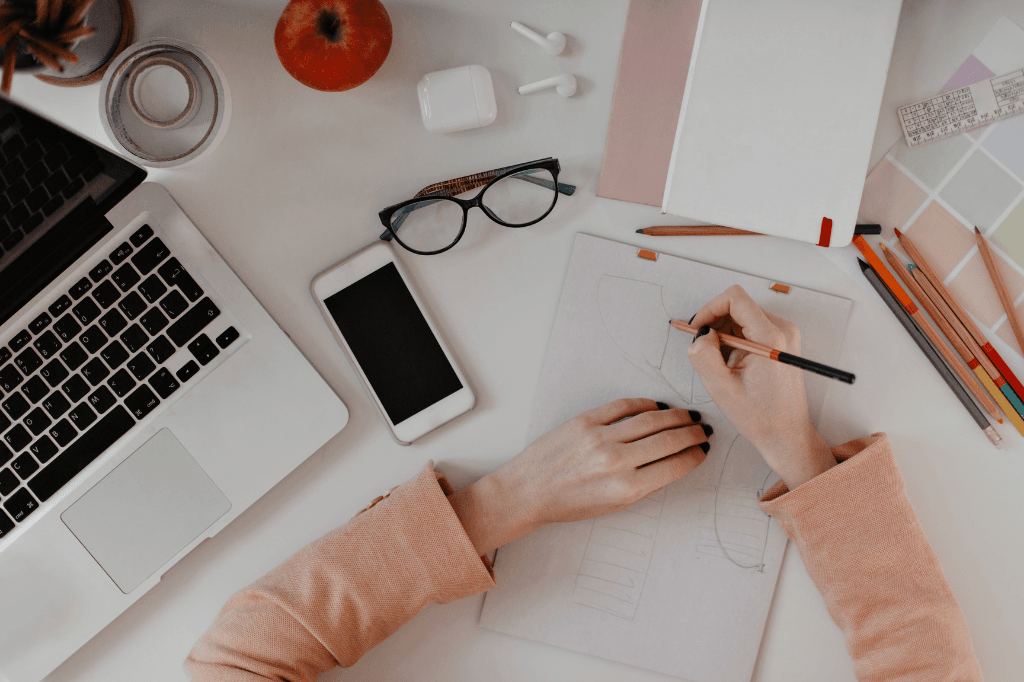 Designer sketching a fashion concept at a workspace with a laptop, smartphone, and creative tools, symbolizing business innovation and retail strategy