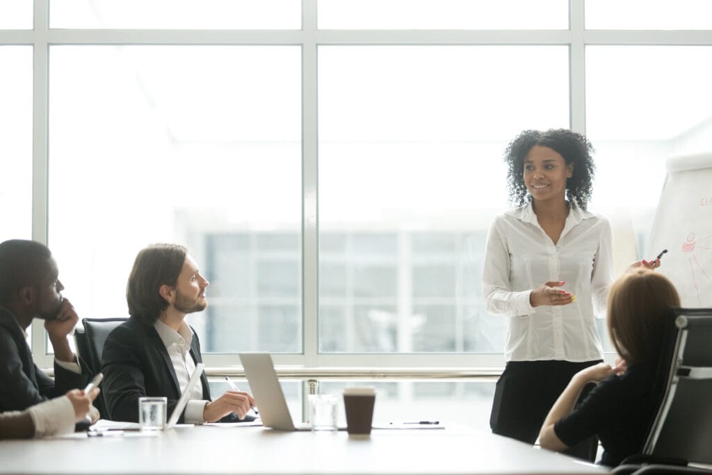 Confident businesswoman giving a presentation to a team in a modern office, representing leadership, strategy, and business development.