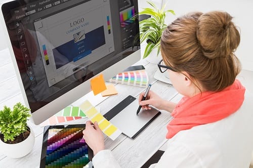 Graphic designer working on a branding project using a digital tablet, color swatches, and a computer screen displaying a logo, representing brand identity and creative strategy