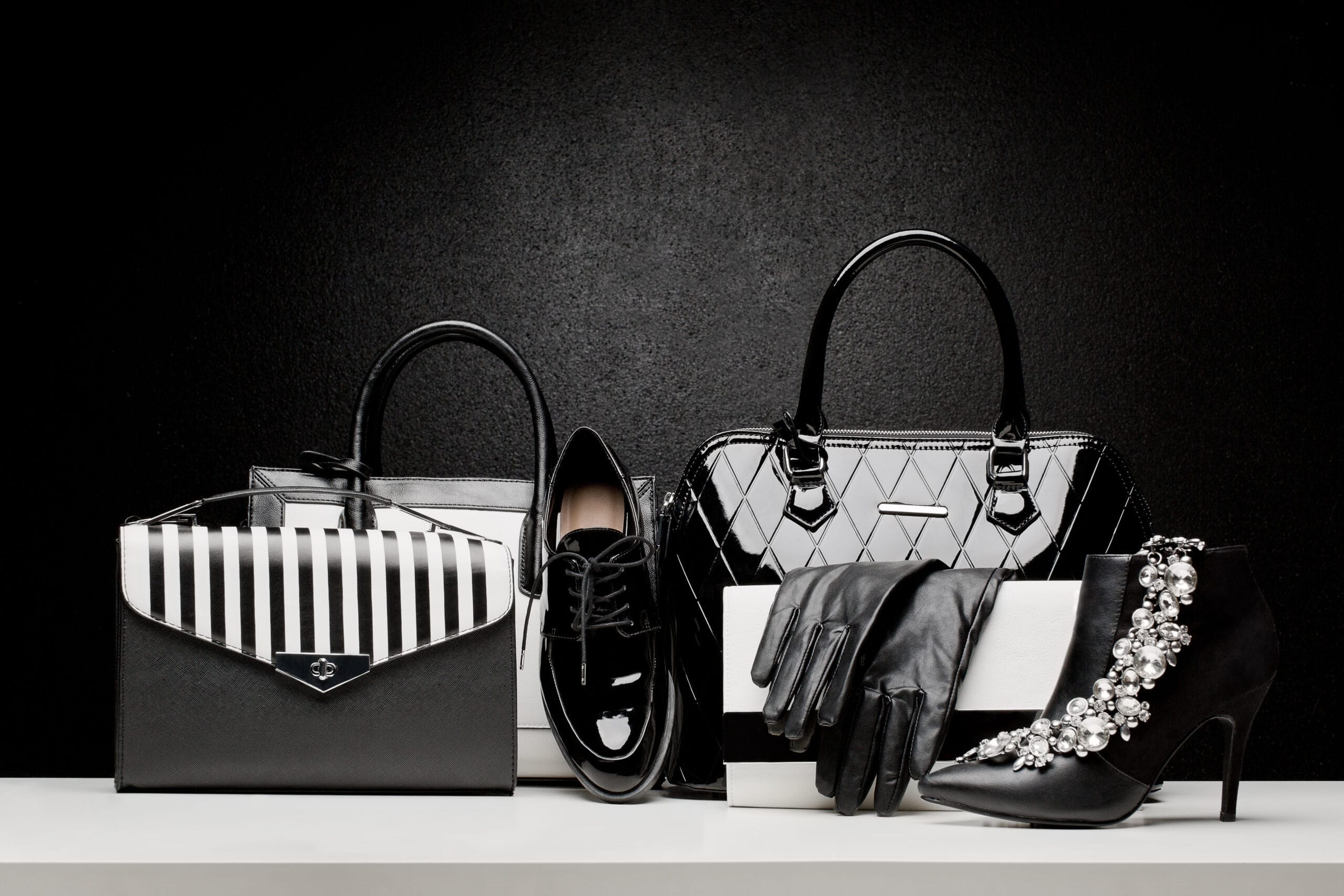 Chic black and white luxury accessories, including designer handbags, patent leather shoes, gloves, and embellished heels, representing high-end fashion retail and premium styling.